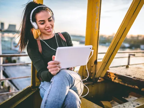 Frau mit Tablet sitzt auf Kran | WINGS-Fernstudium