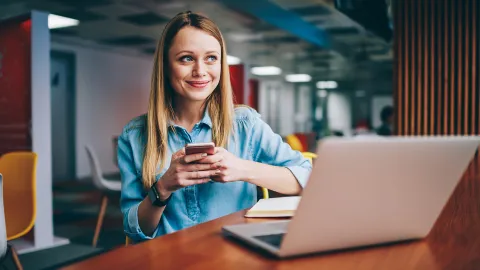 Frau sitzt am Laptop und Handy | WINGS-Fernstudium