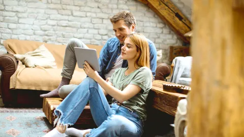 Mann und Frau sitzen im Wohnzimmer mit Tablet | WINGS-Fernstudium